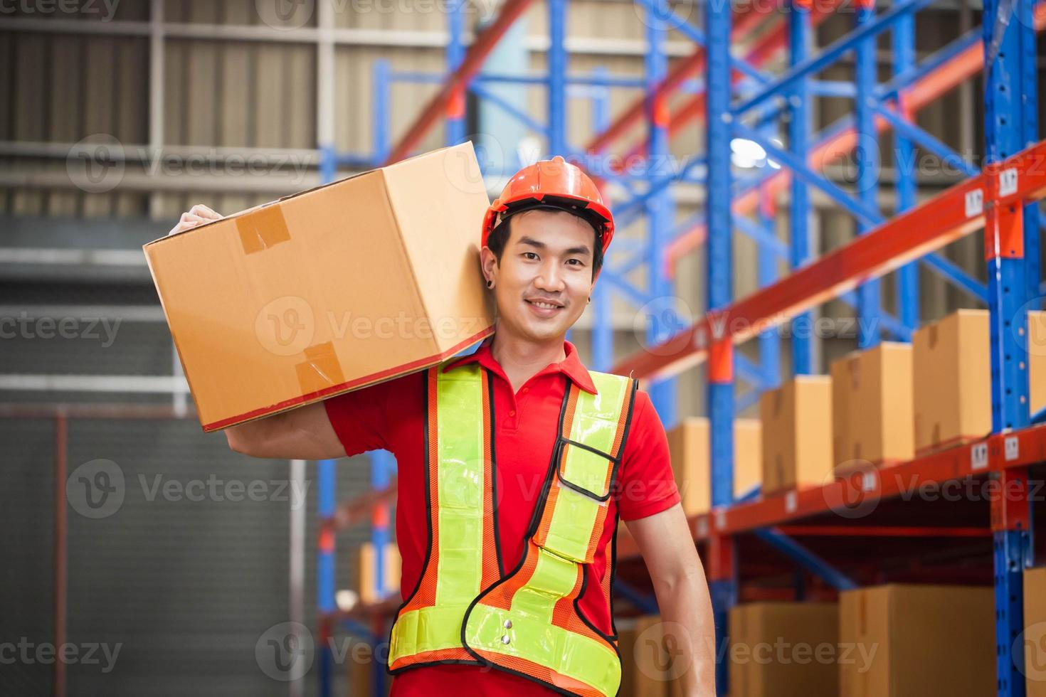 männlich Arbeiter im Helm halten Karton Box Gehen durch im Verkauf Lagerhaus, Warenhaus Arbeiter Arbeiten im Fabrik Warenhaus foto