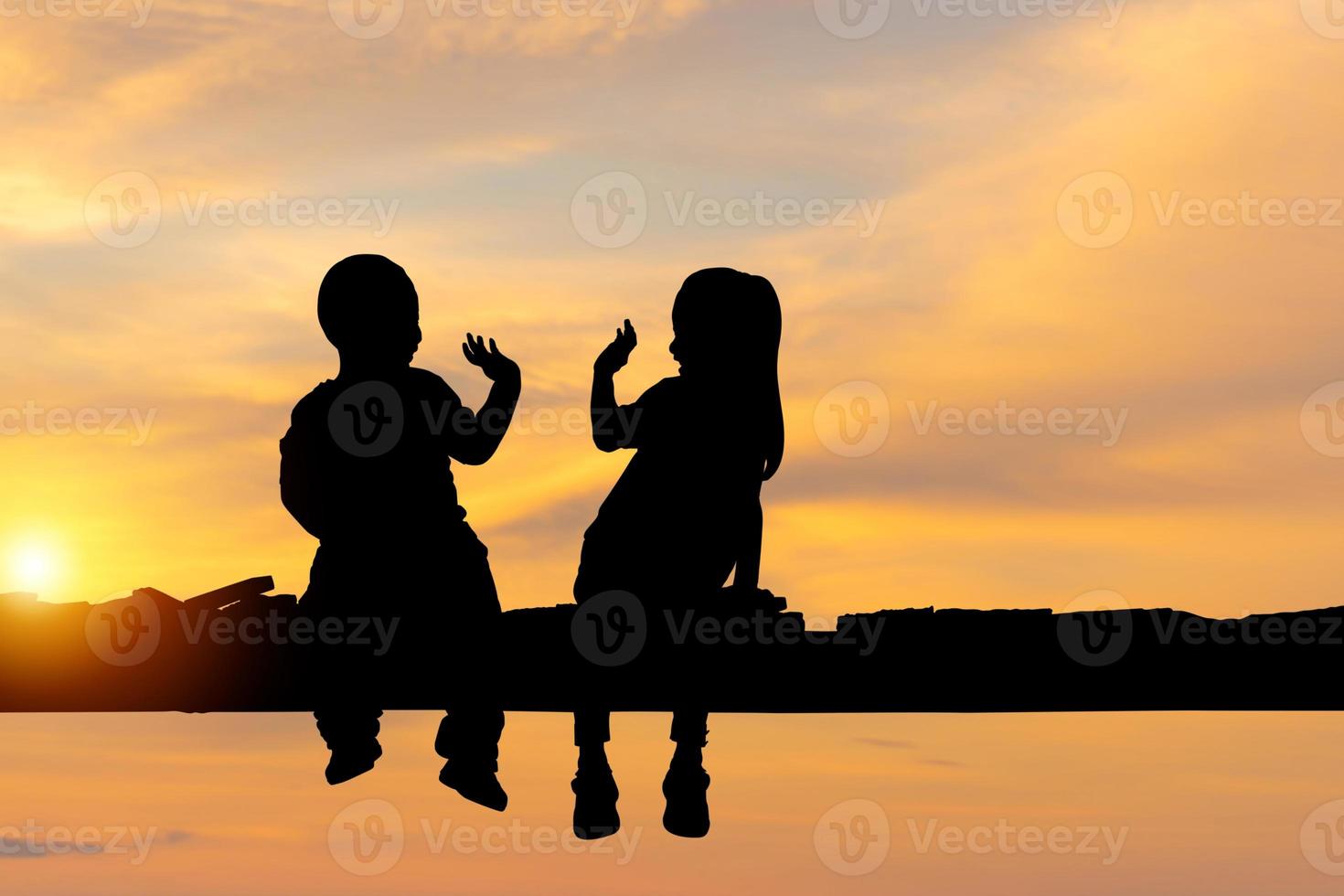 Silhouette von Kinder Sitzung auf das hölzern Brücke, Kinder Junge und Mädchen lesen Buch draussen foto