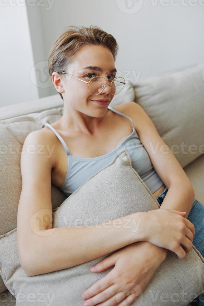 ein Frau tragen Brille sitzt auf ein Couch und sieht aus beim das Kamera. Vision Probleme foto