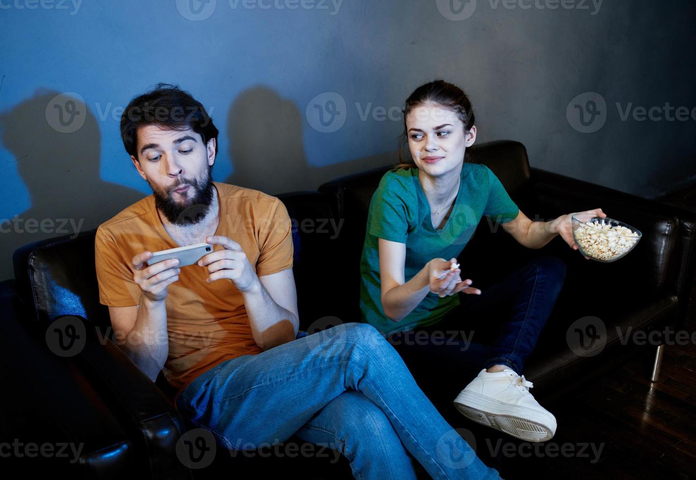 ein Mann mit ein Handy, Mobiltelefon Telefon und ein ziemlich Frau Aufpassen Fernseher drinnen im das Abend foto