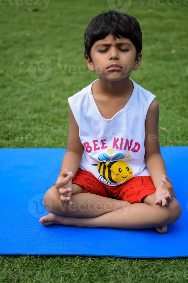 asiatisch Clever Kind tun Yoga Pose im das Gesellschaft Park draussen, Kinder- Yoga Pose. das wenig Junge tun Yoga Übung. foto