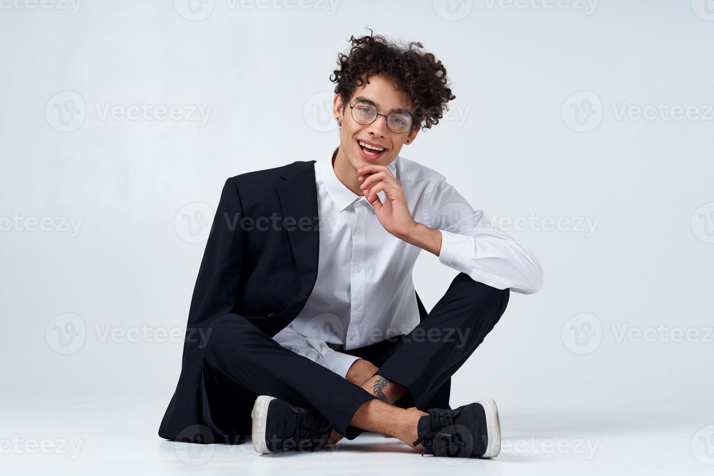 stilvoll jung Mann mit lockig Haar und im ein klassisch passen auf ein Licht Hintergrund drinnen im voll Wachstum foto