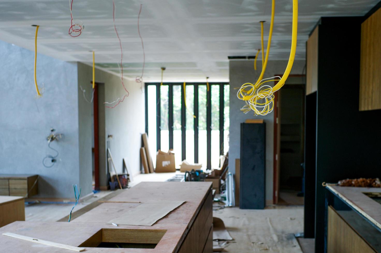 Selektiver Fokus auf von der Decke hängende elektrische Leitungen mit Blick auf das im Bau befindliche Haus foto