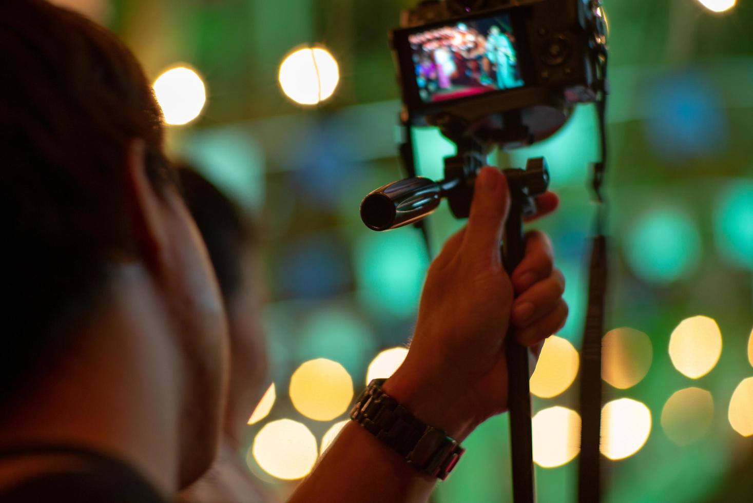 Unscharfer Bewegungsmann, der die Kamera mit Stativ mit funkelnden Bokeh-Lichtern im Hintergrund verwendet foto