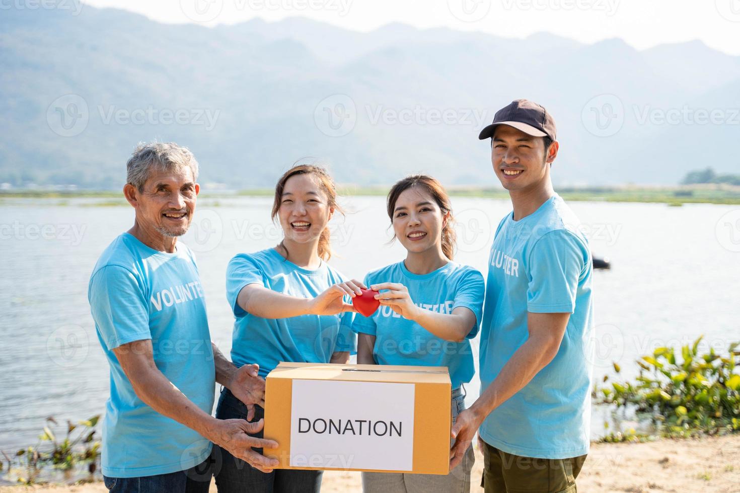 glücklich Mannschaft von Freiwillige halten rot Herz, zeigen Objekt beim Kamera, lächelnd. Mannschaft fördern Wohltätigkeit, Spende Kampagne, Gesundheit Versicherung, medizinisch Untersuchung. foto