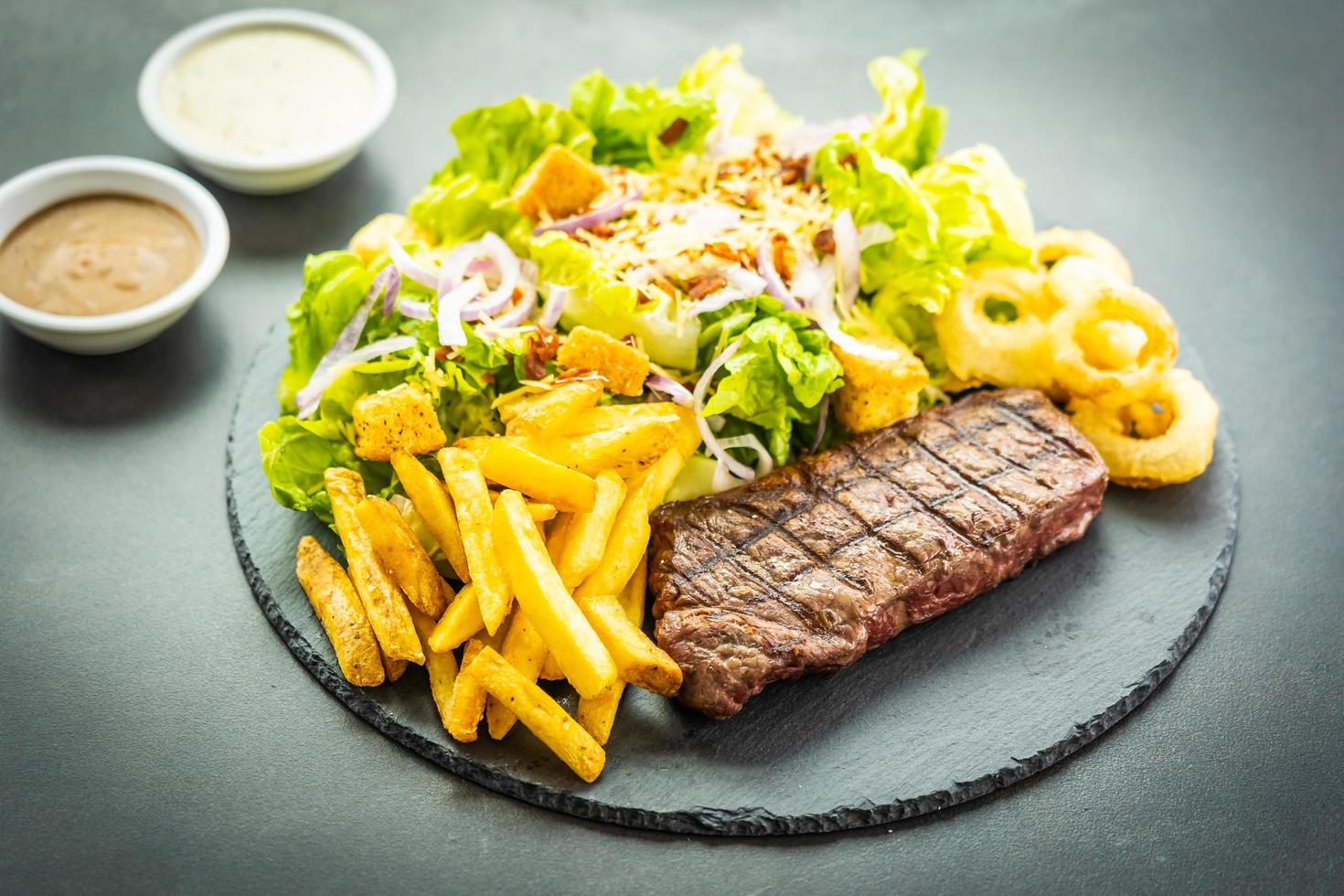 Gegrilltes Rinderfleischsteak mit Pommes Frites Zwiebelring mit Sauce und frischem Gemüse foto