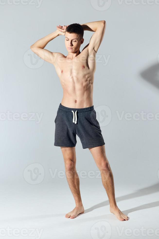 Athlet im kurze Hose mit nackt Torso mit trat bei Hände hinter Kopf auf grau Hintergrund foto