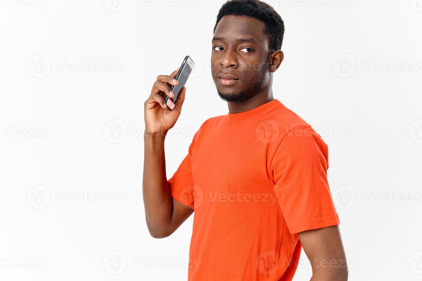 afrikanisch amerikanisch mit Handy, Mobiltelefon Telefon im Orange T-Shirt Neu Technologien foto
