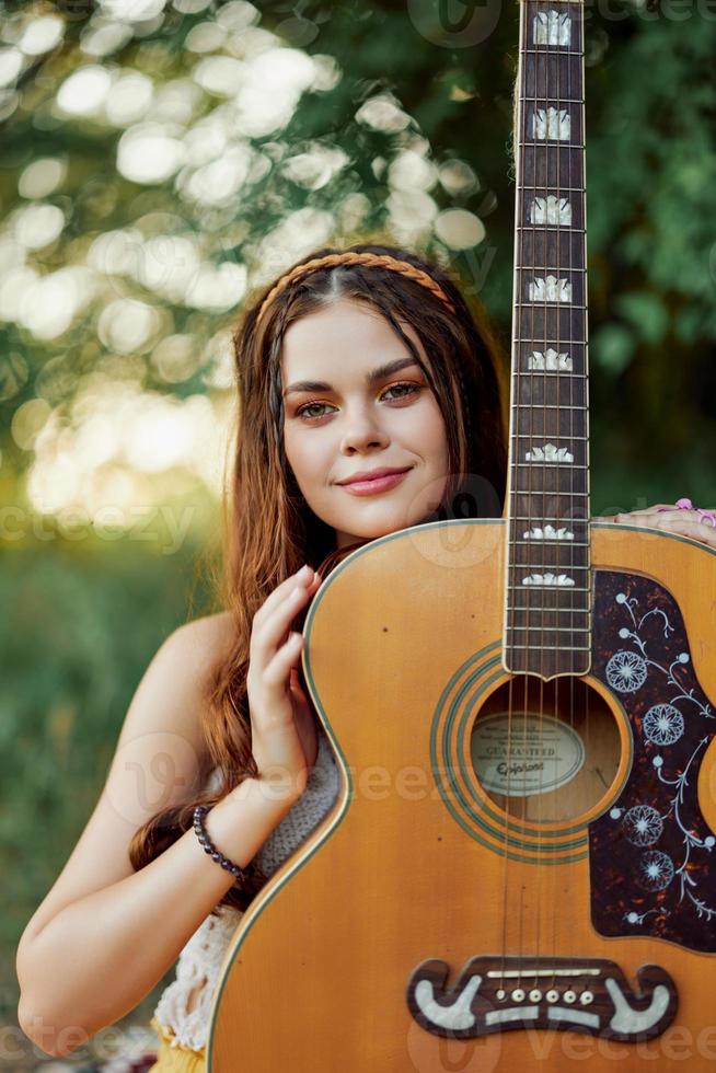 jung Hippie Frau mit Öko Bild lächelnd und suchen in das Kamera mit Gitarre im Hand im Natur auf ein Ausflug foto