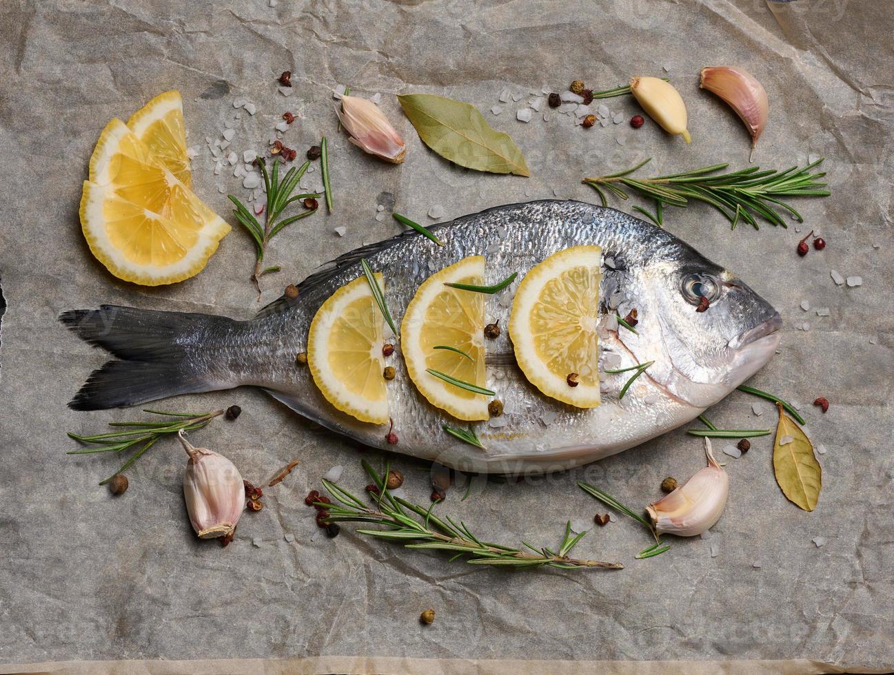 roh ganze Dorado Fisch auf braun Pergament Papier und Gewürze zum Kochen, oben Aussicht auf schwarz Tabelle foto