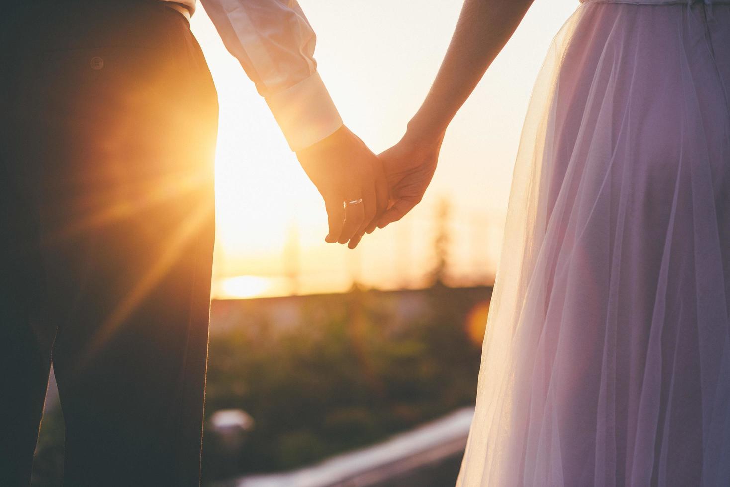 Braut und Bräutigam, die Hände bei Sonnenuntergang halten foto