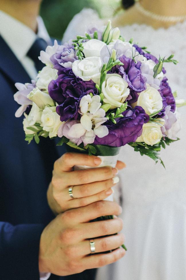 Braut und Bräutigam halten einen weißen und lila Blumenstrauß foto