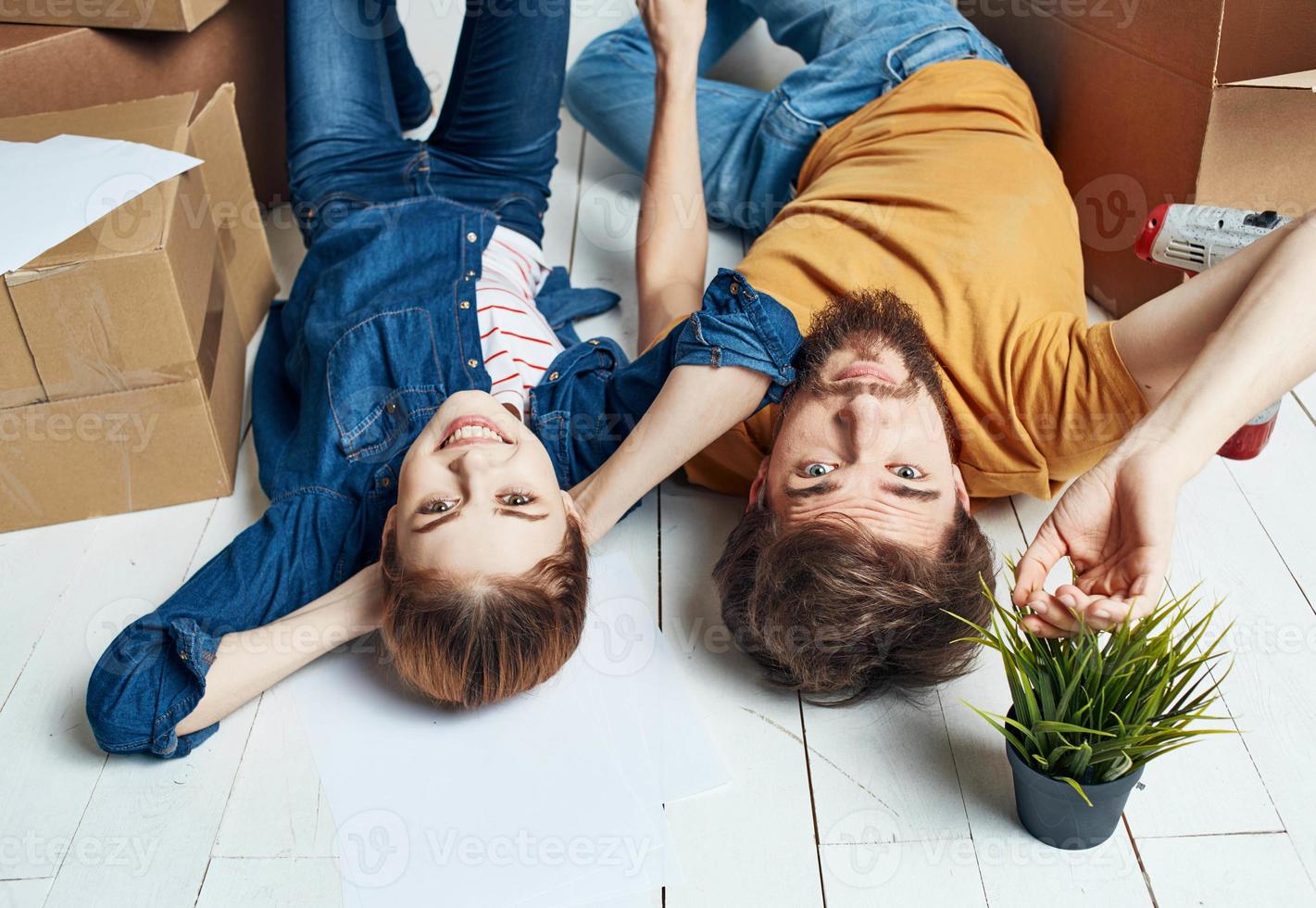 Mann und Frau mit Kisten auf das Fußboden ein Blume im ein Topf ziehen um zu Reparatur Arbeit foto