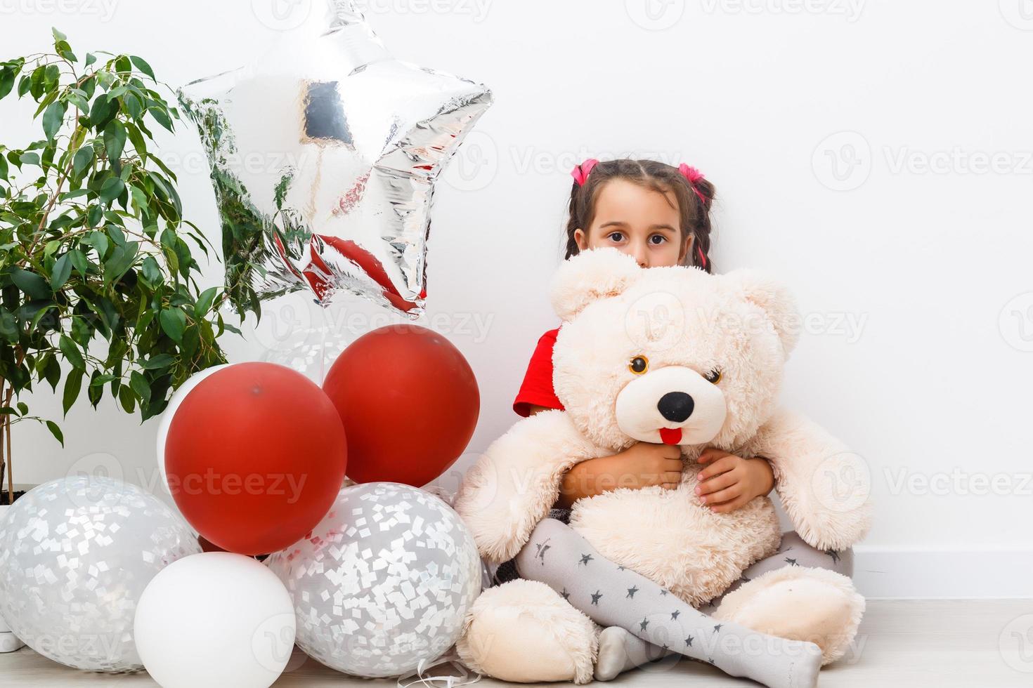Porträt von lächelnd heiter Mädchen liebäugelt mit Teddy Bär im Spiel Zimmer. sie ist phantasieren Über Luft Ballon foto