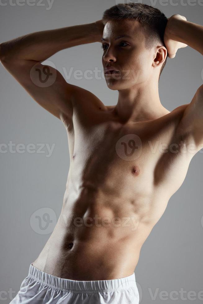 Bodybuilder mit ein aufgepumpt Torso halten seine Hände hinter seine Kopf auf ein grau Hintergrund abgeschnitten Aussicht Porträt foto
