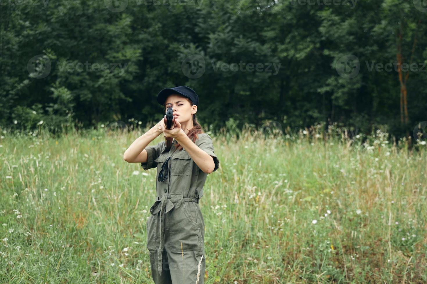 Frau Soldat Frau halten ein Waffe im Vorderseite von ihr Jagd frisch Luft Grün Blätter foto