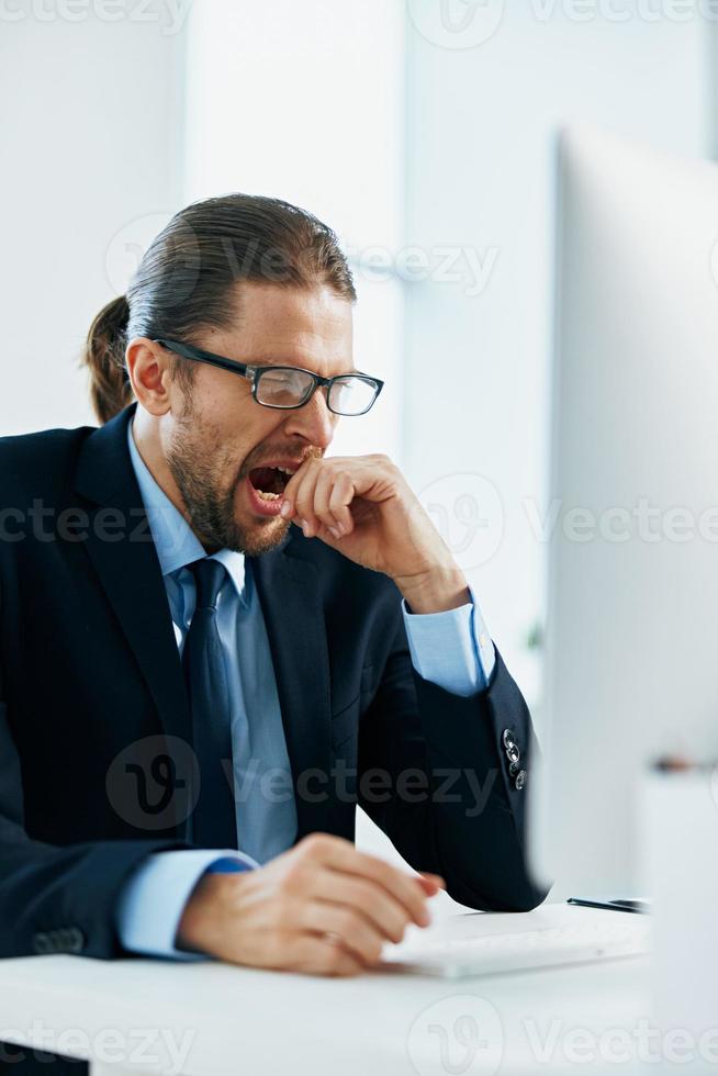 Geschäft Mann im ein passen Sitzung beim seine Schreibtisch müde im Vorderseite von ein Computer foto