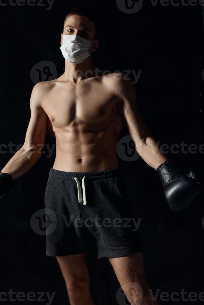 sportlich Mann im medizinisch Maske und im Boxen Handschuhe auf schwarz Hintergrund foto