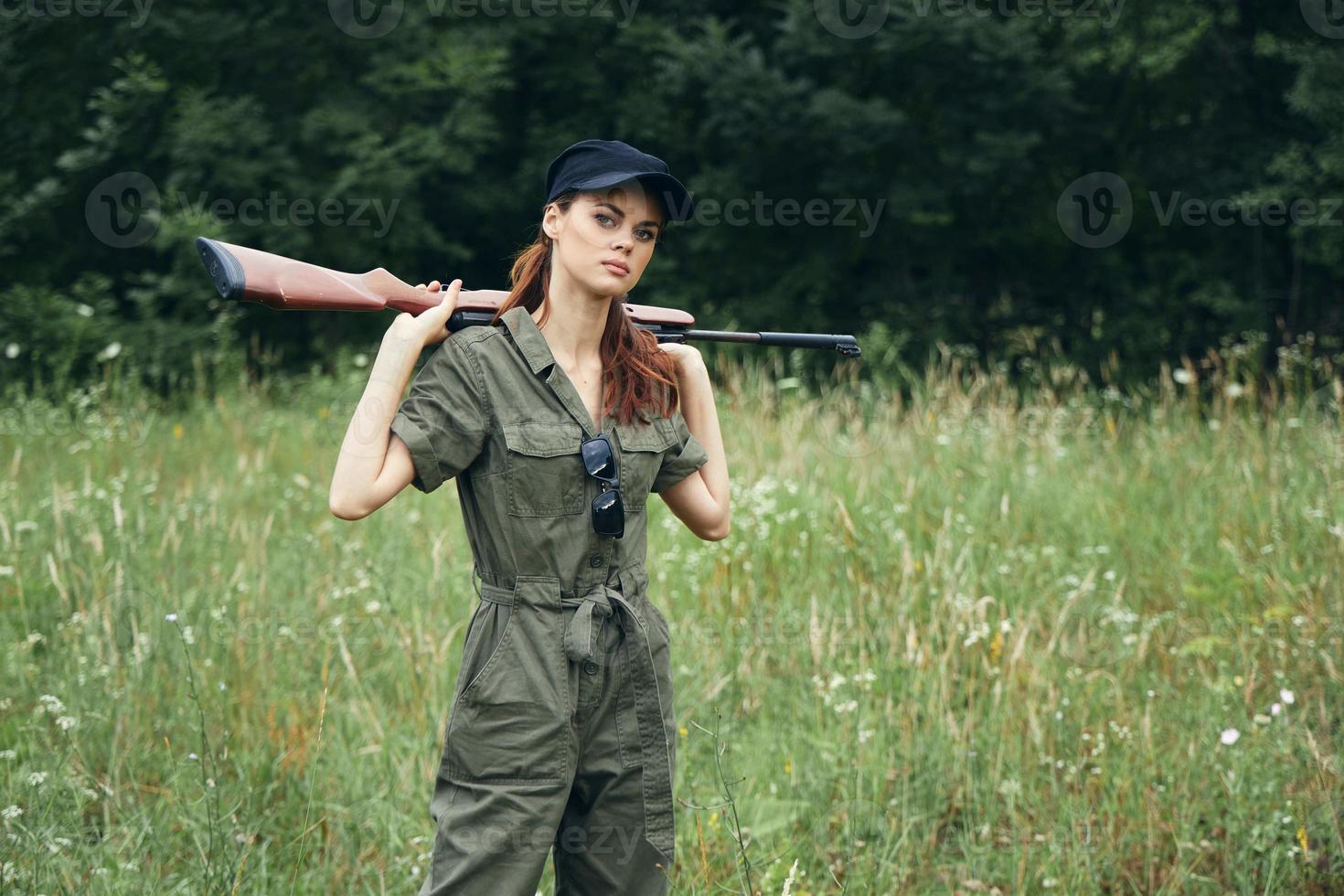 Frau Soldat im ein Grün Overall hält Waffen auf seine Schultern ein Lebensstil Grün Blätter foto