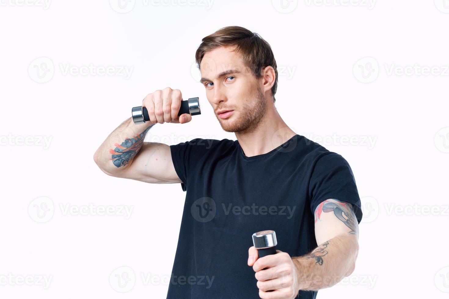 sportlich Mann im ein schwarz T-Shirt mit Hanteln im seine Hände auf ein Weiß Hintergrund foto