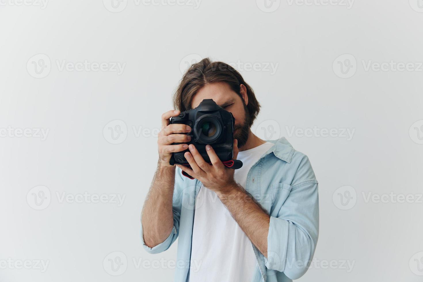 ein männlich Hipster Fotograf im ein Studio gegen ein Weiß Hintergrund sieht aus durch das Kamera Sucher und schießt Schüsse mit natürlich Licht von das Fenster. Lebensstil Arbeit wie ein freiberuflich Fotograf foto