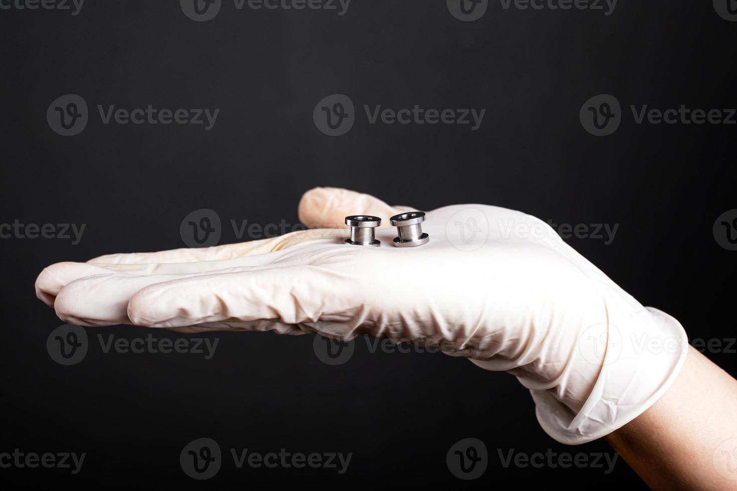 Hand in einem weißen Einweghandschuh hält durchdringende Tunnel auf einem dunklen Hintergrund foto