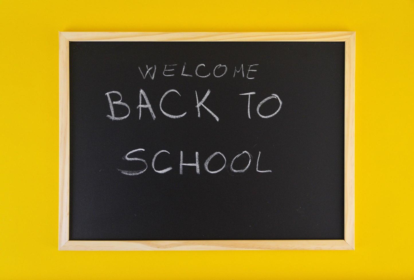handgezeichneter Titel Willkommen zurück in der Schule auf schwarzer Tafel unter gelbem lebendigem Hintergrund. foto