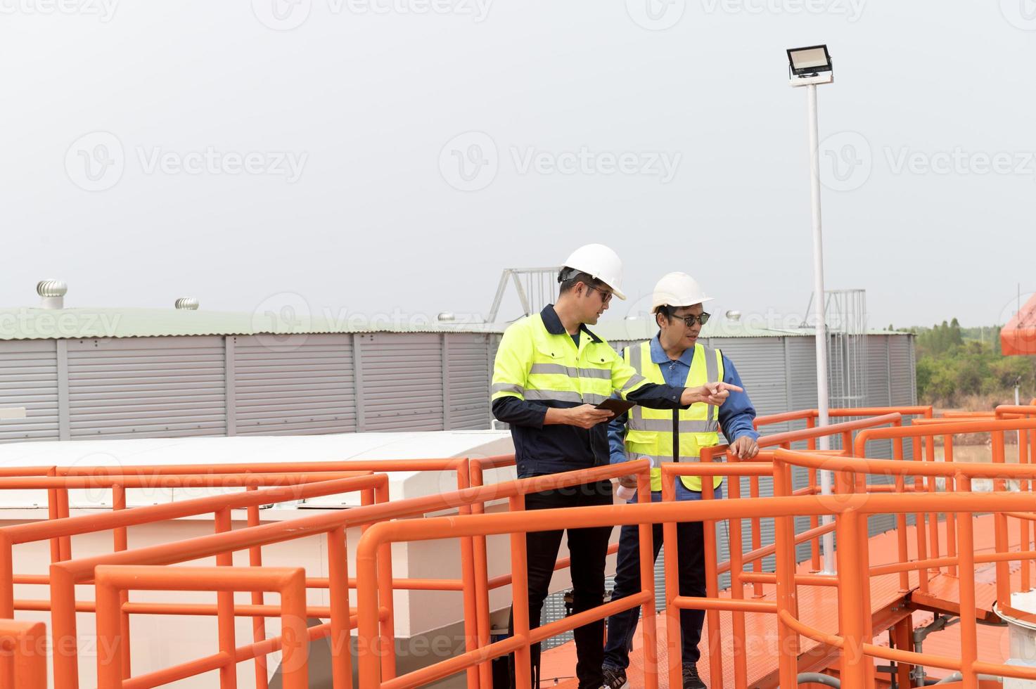 zwei schwer industriell Ingenieure Stehen im ein Standard Wasser Behandlung Pflanze verwenden Digital Tablette Computers und chatten. asiatisch Industrie Profis foto