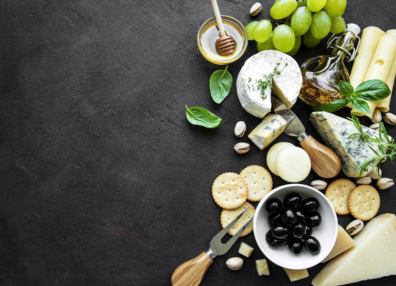 verschiedene Arten von Käse, Trauben, Honig und Snacks auf einem schwarzen Betonhintergrund foto