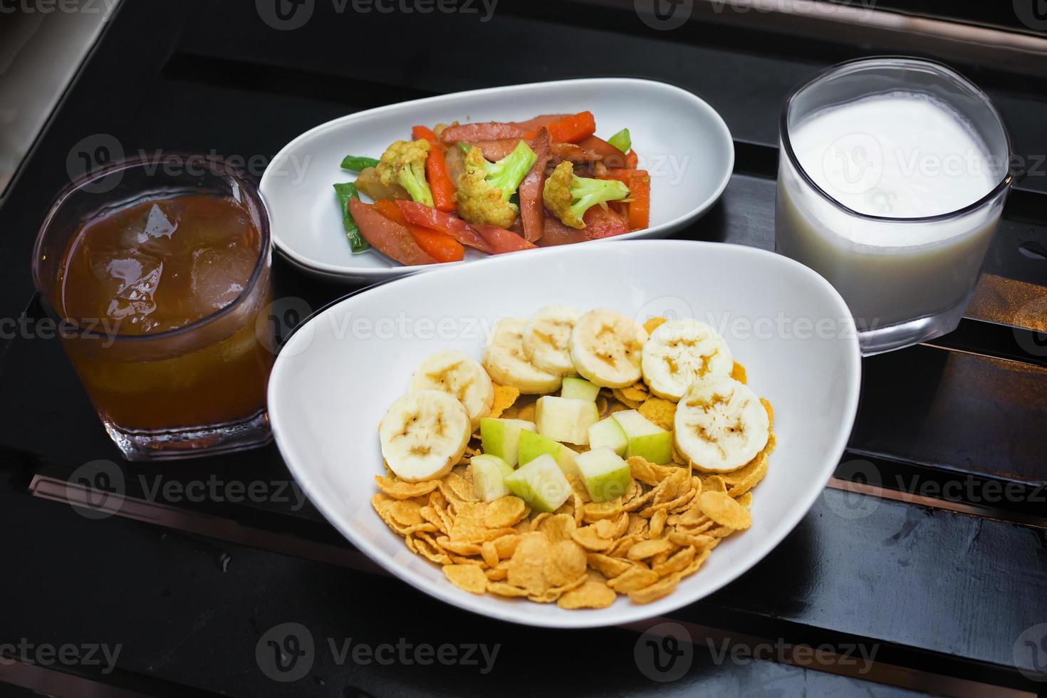 kontinental Frühstück Cornflakes mit Früchte, Milch und Tee und etwas von anbraten Gemüse auf schwarz Holz Tisch. oben Sicht. foto