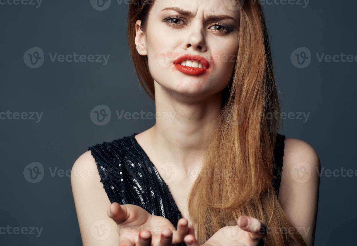 ein Frau im ein schwarz Kleid mit rot Lippen Gesten mit ihr Hände verwirrt aussehen grau Hintergrund foto