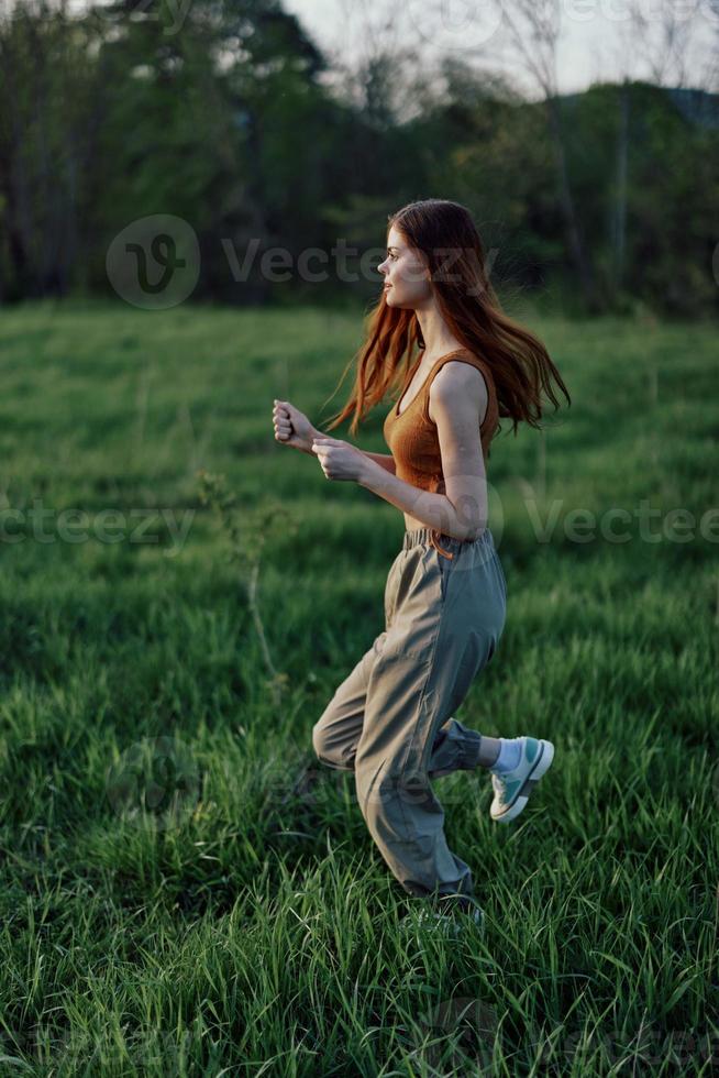 ein jung Frau ausüben draußen und Laufen im das Park. im das Abend auf das Grün Gras in das Sonnenuntergang foto