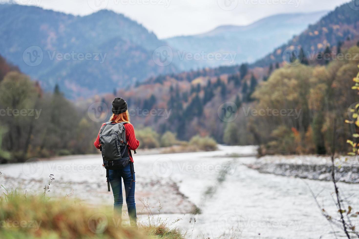 Frau im ein rot Sweatshirt mit ein Rucksack im das Berge auf Natur in der Nähe von das Fluss Teich See foto