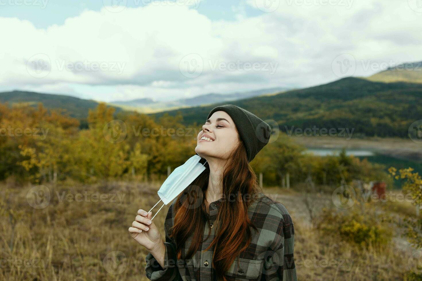 glücklich Frau Wanderer mit medizinisch Maske lächelnd auf Natur im das Park im das Berge foto