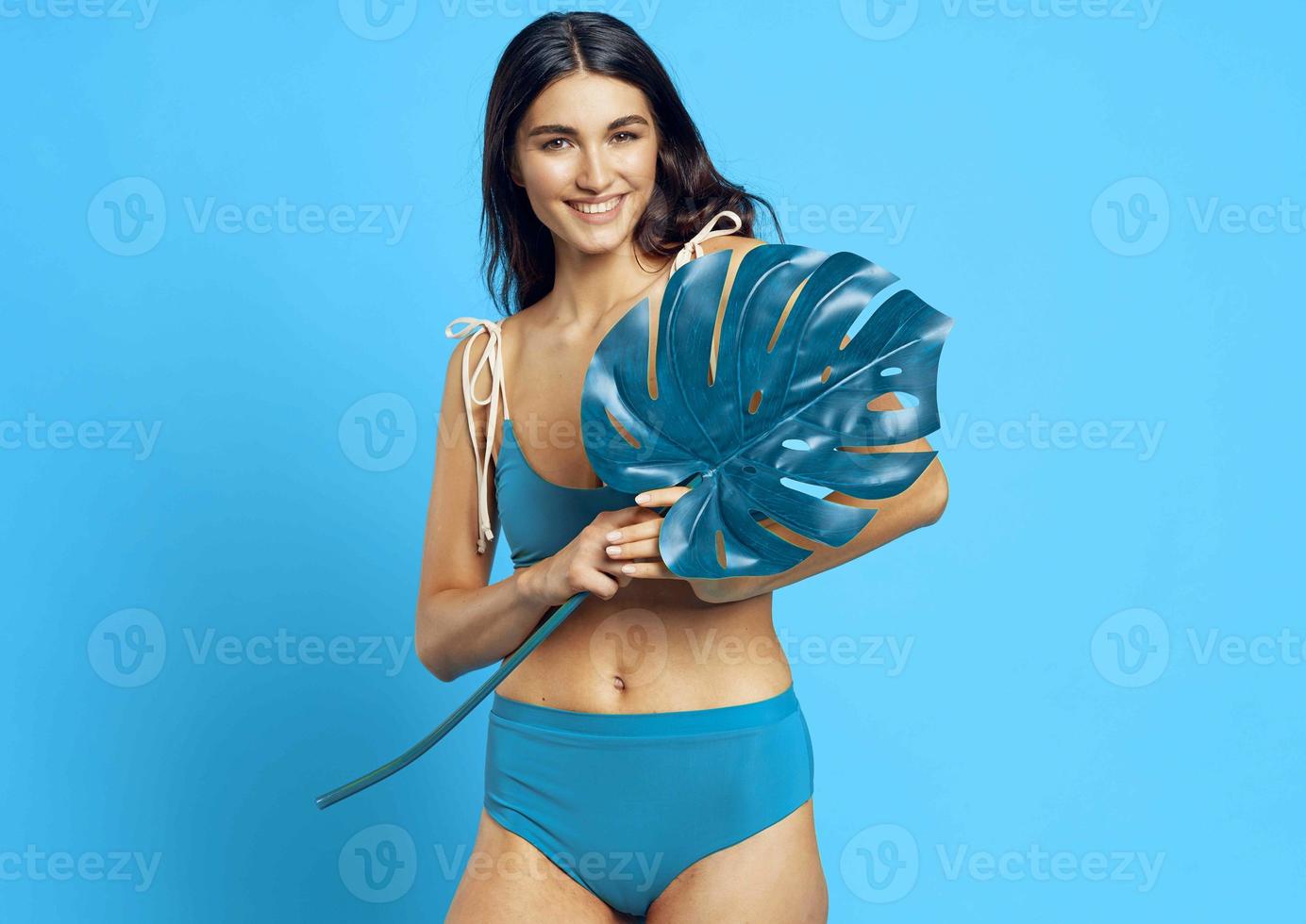 heiter Frau im ein Blau Badeanzug Palme Blatt exotisch Blau Hintergrund foto