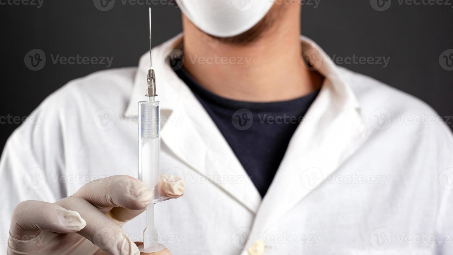 Arzt in einem weißen Kittel mit Handschuhen und einer medizinischen Maske hält eine Spritze mit medikamentöser Behandlung zur Vorbeugung von Krankheiten foto