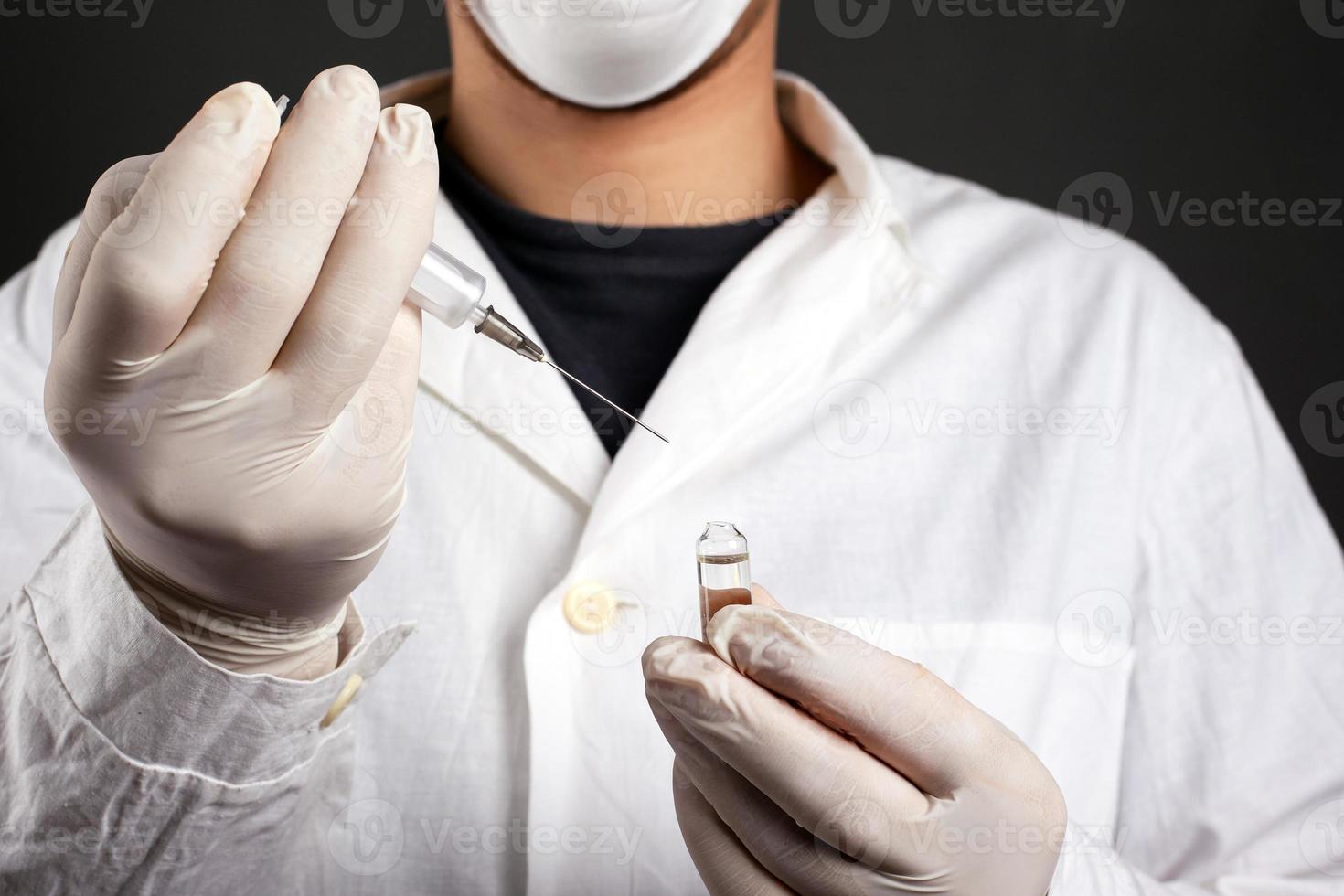 Arzt in einem weißen Kittel mit Einweghandschuhen und einer Maske mit einer Spritze foto