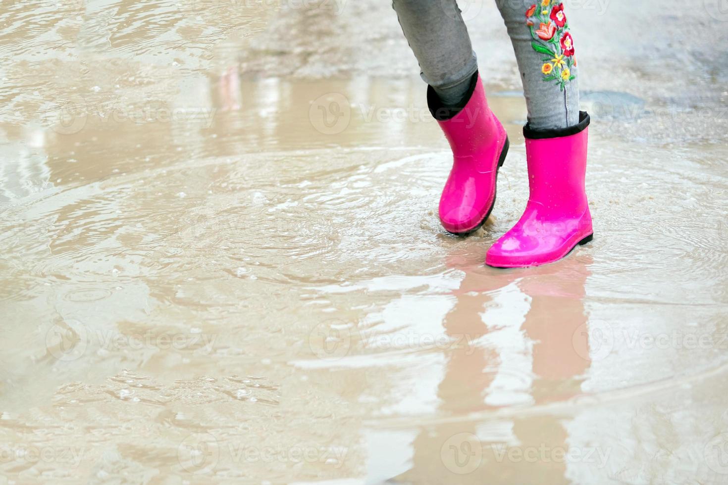 Nahansicht von Baby Füße im Rosa Gummi Stiefel im ein Pfütze. das wenig Mädchen fühlt sich geschützt von das Regen im Rosa Stiefel. foto