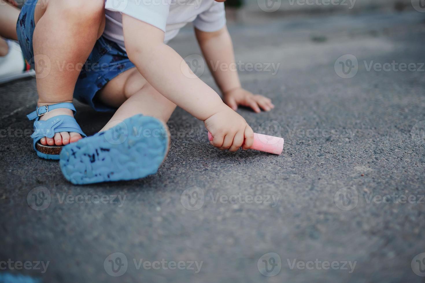 Nahaufnahme eines kleinen Mädchens, das mit Kreide auf dem Bürgersteig zeichnet. Kinder zeichnen mit Kreide foto