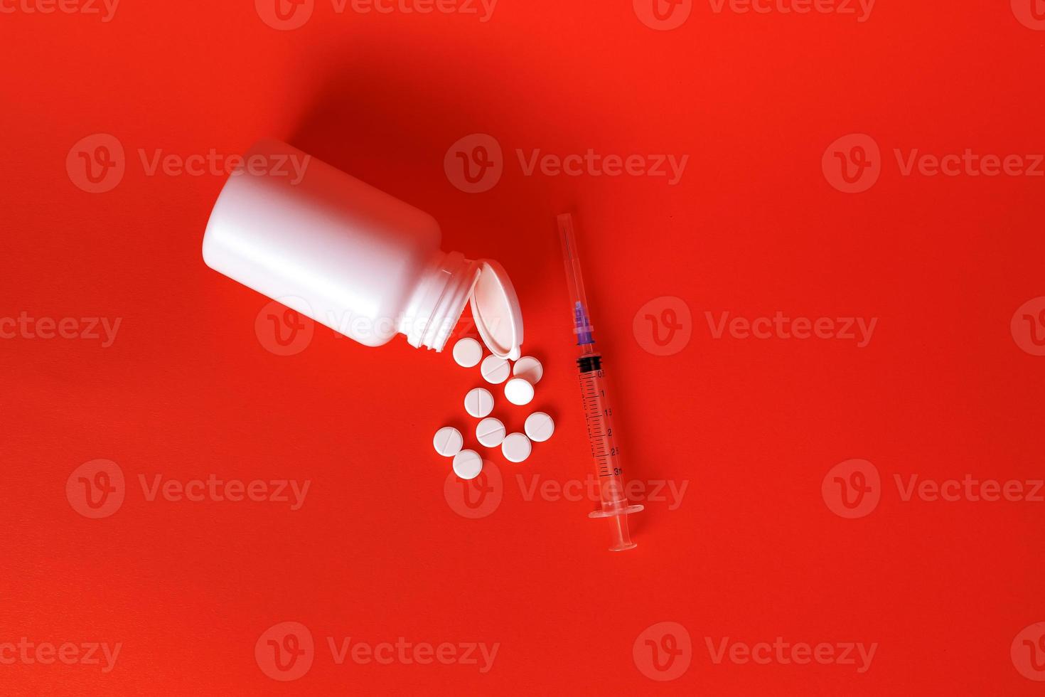 weiße Pillen verstreut in einem weißen Glas und einer Spritze auf einem roten Hintergrund. selektiver Fokus. Konzept der Gesundheit. foto