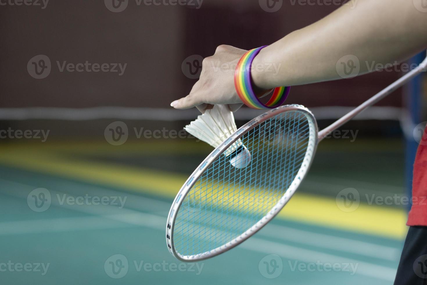 Badminton Spieler trägt Regenbogen Armbänder und halten Schläger und Weiß Federball im Vorderseite von das Netz Vor Portion es zu Spieler im Ein weiterer Seite von das Gericht, Konzept zum lgbt Menschen Aktivitäten. foto