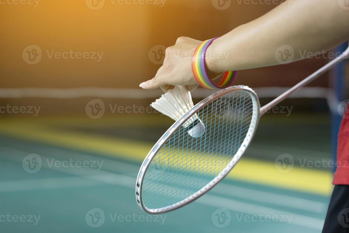 Badminton Spieler trägt Regenbogen Armbänder und halten Schläger und Weiß Federball im Vorderseite von das Netz Vor Portion es zu Spieler im Ein weiterer Seite von das Gericht, Konzept zum lgbt Menschen Aktivitäten. foto