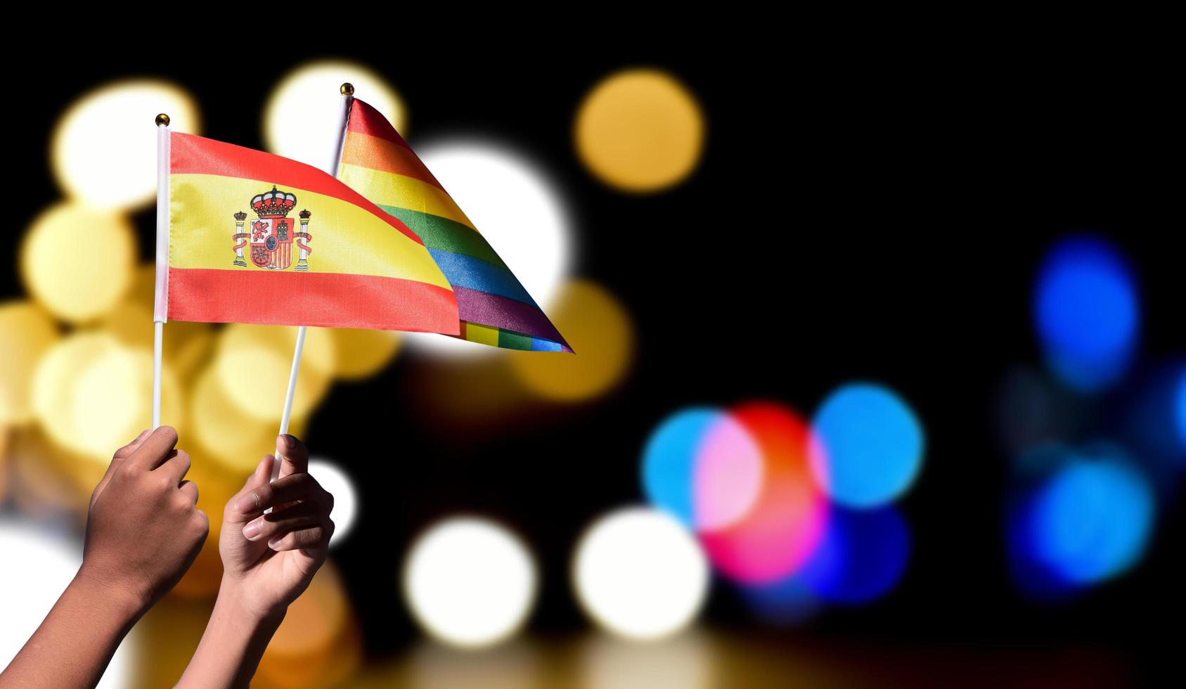 Spanien Flagge und Regenbogen Flagge halten im Hand mit verschwommen Straße Licht Bokeh Hintergrund', Konzept zum feiern von lgbt Menschen im Spanien im Stolz Monat, Juni. foto