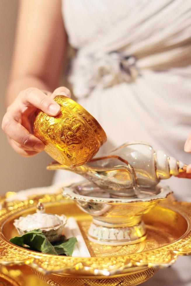 Frau Hand hoding Gold Tasse zum gießen Wasser im Muschel Schale auf glod Tablett im Tradition thailändisch Hochzeit Zeremonie foto