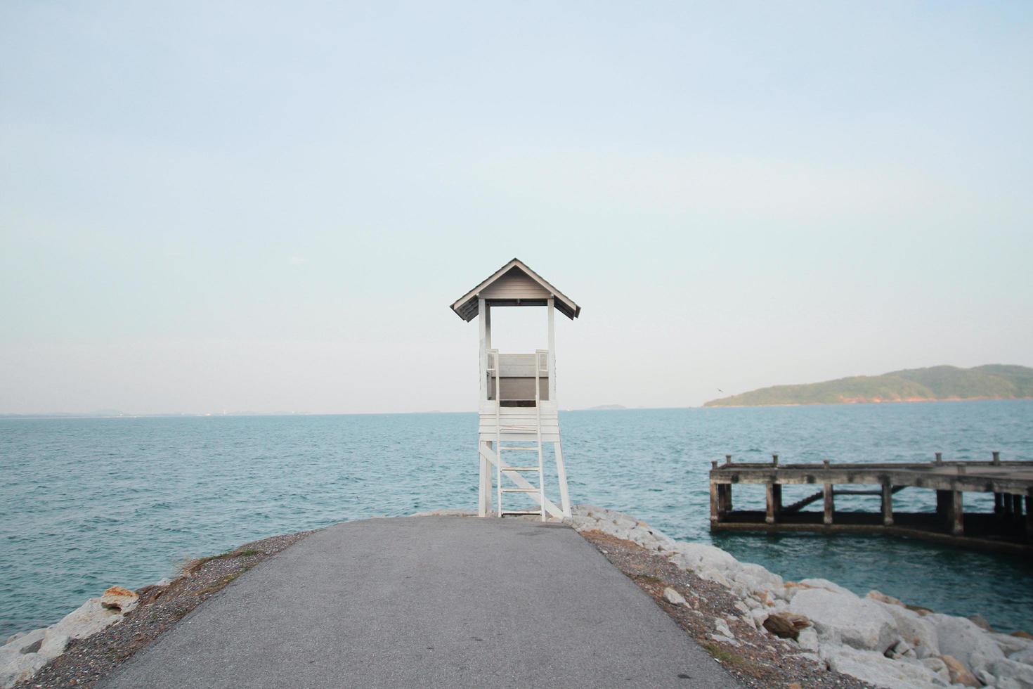 Weiß Rettungsschwimmer Turm und alt hölzern Brücke mit Seelandschaft Aussicht auf das Strand im Thailand foto