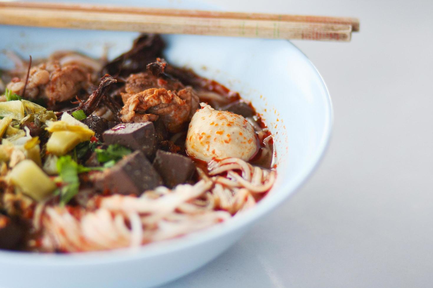 Reis Nudeln mit würzig Schweinefleisch Soße im Weiß Schüssel mit Essstäbchen und Löffel. thailändisch würzig Lebensmittel. foto