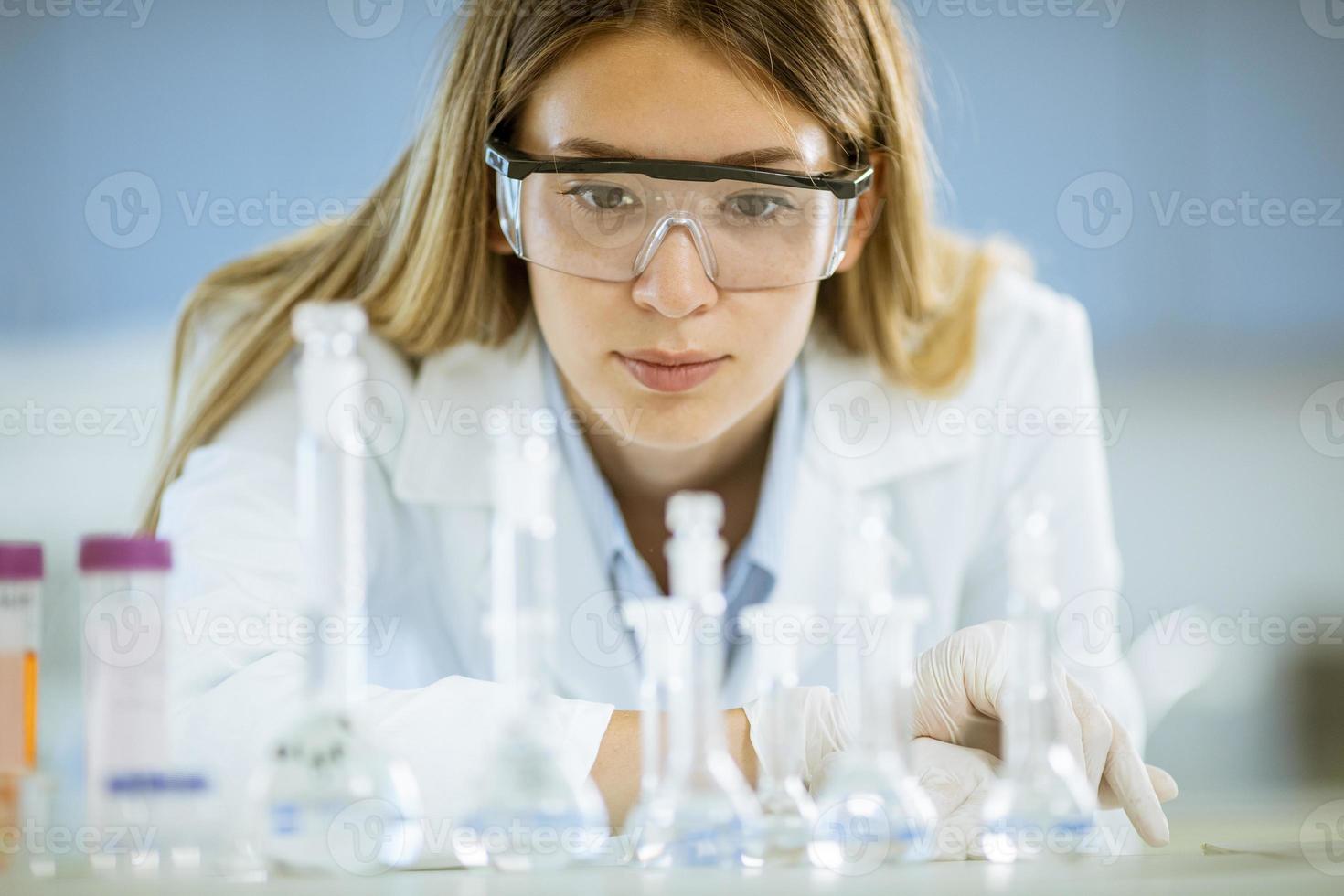 Ärztin oder wissenschaftliche Forscherin, die einen Kolben mit Lösungen in einem Labor betrachtet foto