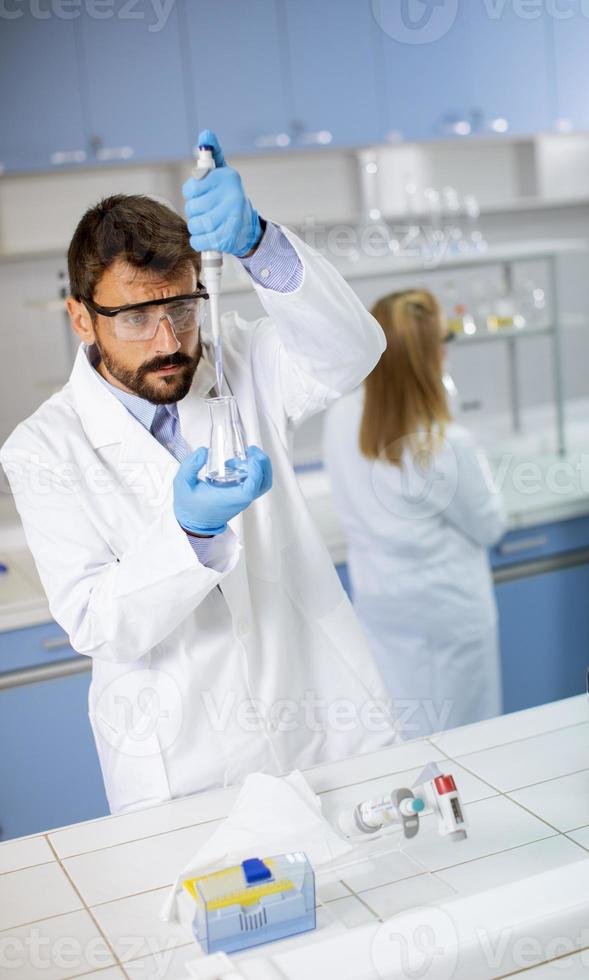 junger Forscher in Arbeitsschutzkleidung, der im Labor steht und den Kolben mit Flüssigkeit analysiert foto