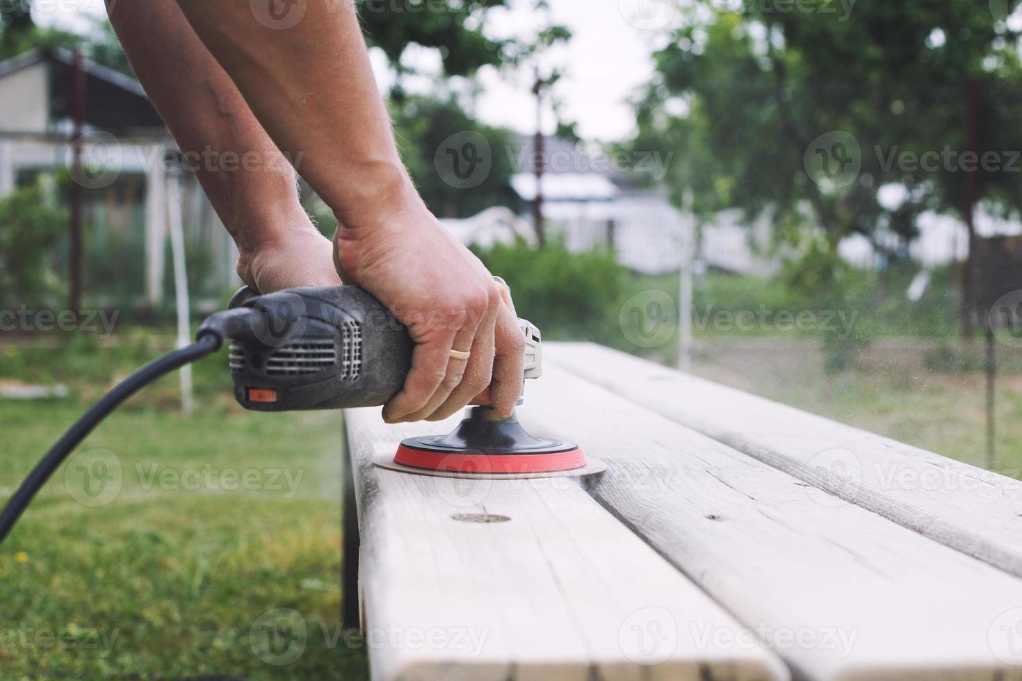 Mann poliert das Tafel auf das Bank. Mann reparieren Bank im das Garten foto