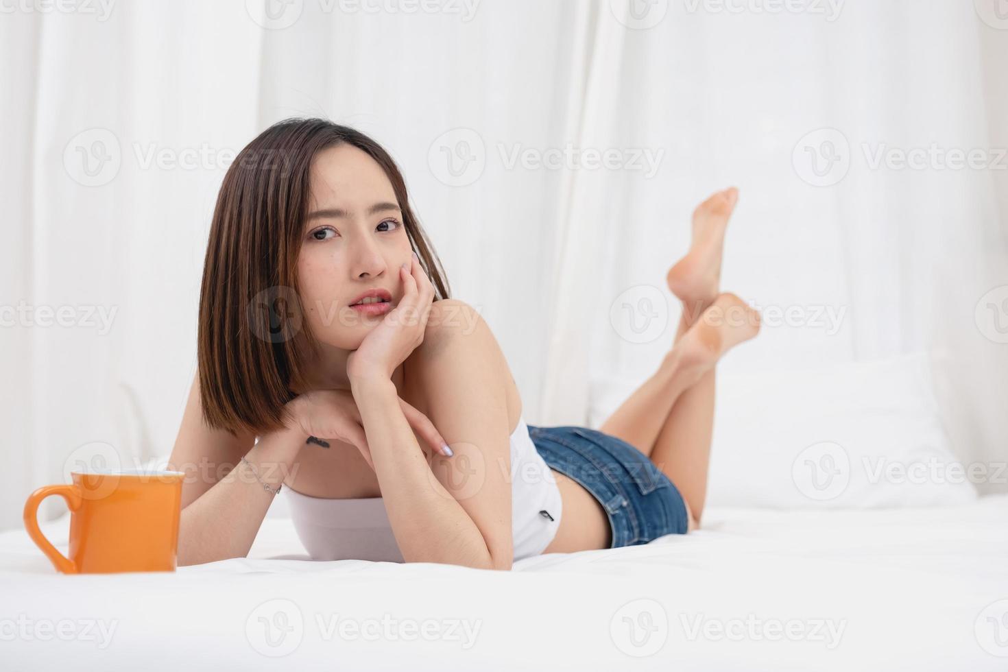 Porträt von Weiß asiatisch Frau mit tätowieren ruhen im Bett zu sich ausruhen und entspannen Innerhalb Weiß Schlafzimmer auf ihr Urlaub, Urlaub Morgen Konzept. foto